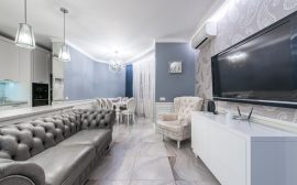 Modern light room with couch and TV on wall near armchair furnished with table and chairs next to cabinets