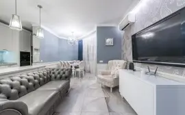 Modern light room with couch and TV on wall near armchair furnished with table and chairs next to cabinets