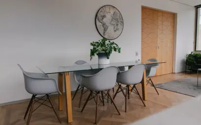 Elegant dining area with glass table, white chairs, parquet flooring, and wall decor.